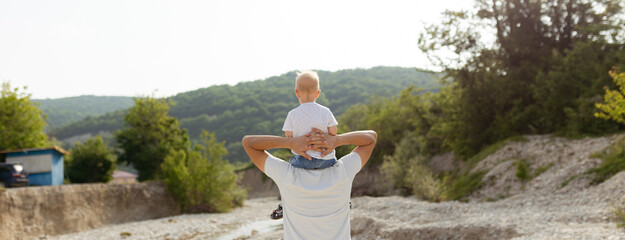 Portrait of happy father giving son piggyback ride on his shoulders. Cute boy with dad playing...