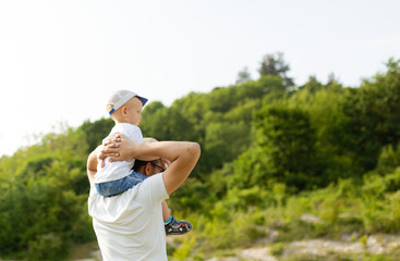 Portrait of happy father giving son piggyback ride on his shoulders. Cute boy with dad playing outdoor
