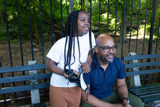 An African-American man and his young daughter sitting on a bench in the park