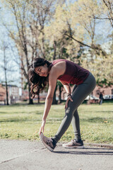 Attractive smiling indian young woman runner stretching calves muscles before running in park