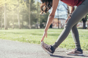 unrecognizable brunette young woman runner stretching calves muscles before running in park, copy space © Alberto