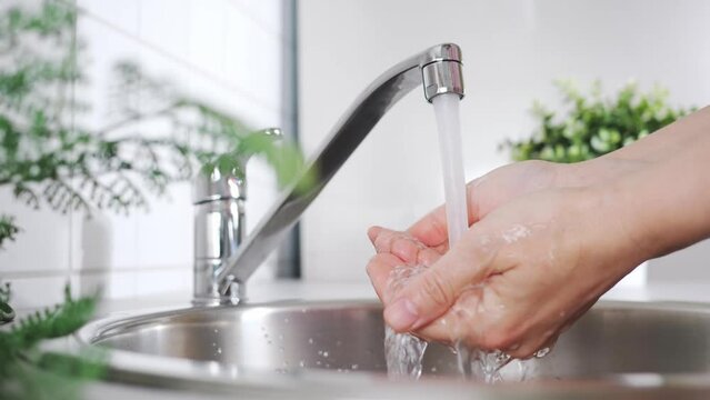 Woman washes her hands under a running water. A stream of clean drink water flows into the kitchen sink. Wash hands and hygiene. Water consumption, environment, pollution and scarcity concept