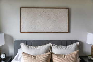 Wall art hanging above a bed with throw pillows in a bedroom