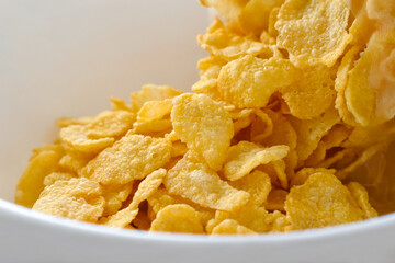 Cornflakes spilling out of a plastic bag in a white bowl. 