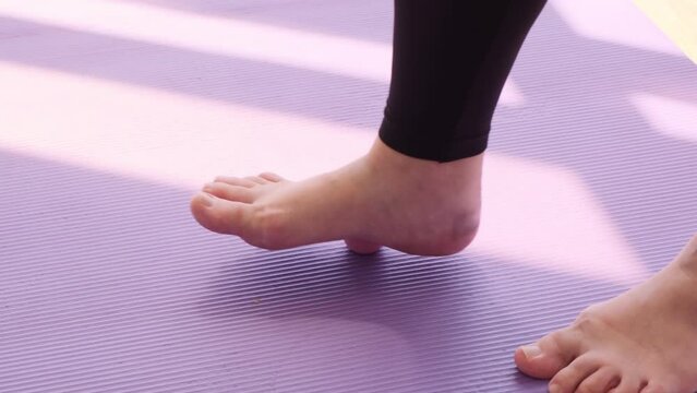 Female legs with red nails roll a small sports ball on the floor close-up. On a purple yoga mat
