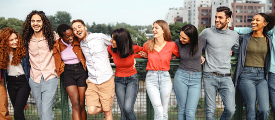 Fototapeta premium Group of 20s multiethnic young friends hugging in the park talking and joking together - multicultural people standing hands on shoulders together - people lifestyle concept
