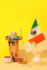 Glass of tasty margarita cocktail, shaker, sombrero and flag of Mexico on color background