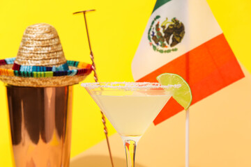 Glass of tasty margarita cocktail, shaker, sombrero and flag of Mexico on color background, closeup