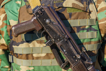 Automatic rifle without a magazine on the back of a military man. Background with selective focus...