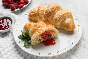Plate of delicious croissants with raspberry jam on light background