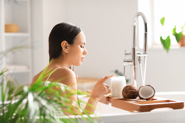 Young woman with jar of coconut oil in bathroom