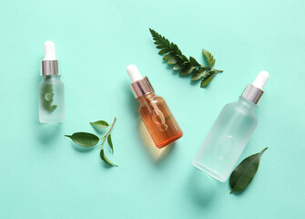Bottles of natural serum and plant leaves on color background
