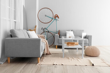 Interior of light living room with bicycle, grey sofas and table