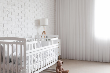 Obraz na płótnie Canvas Baby crib and teddy bear near white brick wall