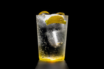 Large glass of gin and tonic, sparkling water, tonic soda with ice and a slice of lemon with a dark...