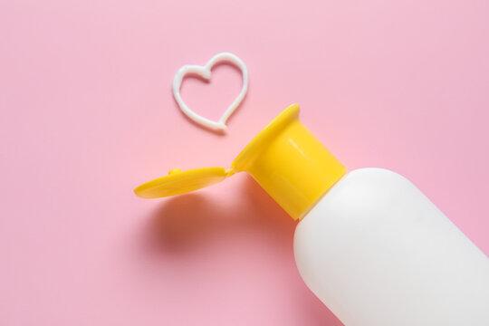 Bottle of sunscreen and heart made of cream on pink background