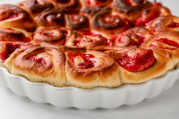 Baking dish with strawberry cinnamon rolls on white background, closeup
