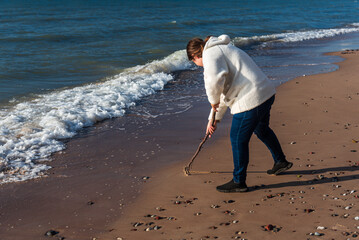 A woman writes in the sand with a branch.