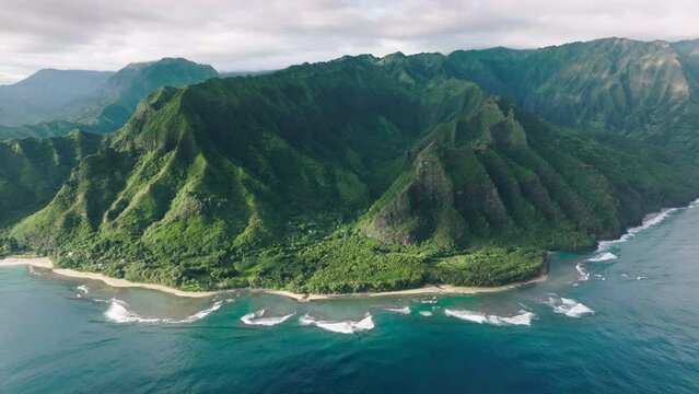 Cinematic green mountain landscape of wild island nature. Wonderful fresh deep blue ocean waves at high green peaks formations with steep green walls. Panoramic aerial of scenic tropical Hawaii nature