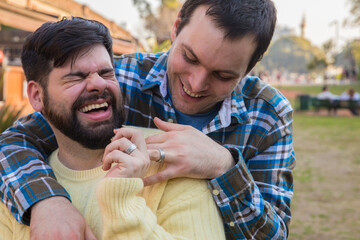 Happy gay couple laughing while holding hands with affection outdoors. LGBTQ, diversity, inclusive...