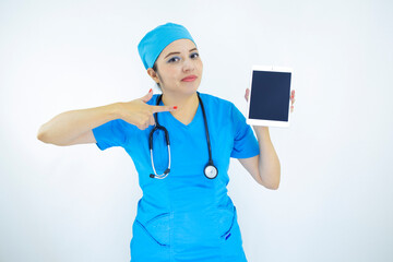 beautiful woman doctor, wearing uniform and blue surgical cap, stethoscope on her neck, pointing at the tablet on white background