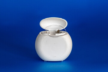 White round open case with white dental floss on a blue background. Plastic box.