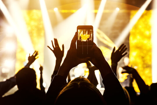 The fan holding his smart mobile phone and photographing a rock concert.
