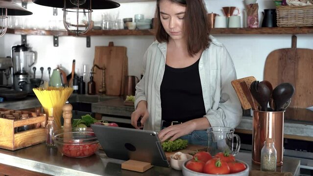 Pretty young woman cooking dietary meal from fresh vegetables browse online recipe on tablet. Caucasian lady modern day housewife enjoy culinary at home in modern kitchen. 4k footage