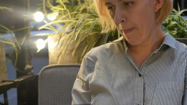An attractive caucasian woman sits at a table in a street restaurant in the evening and studies the menu for ordering dinner. The warm light of the lamp illuminates the face and hair of a woman