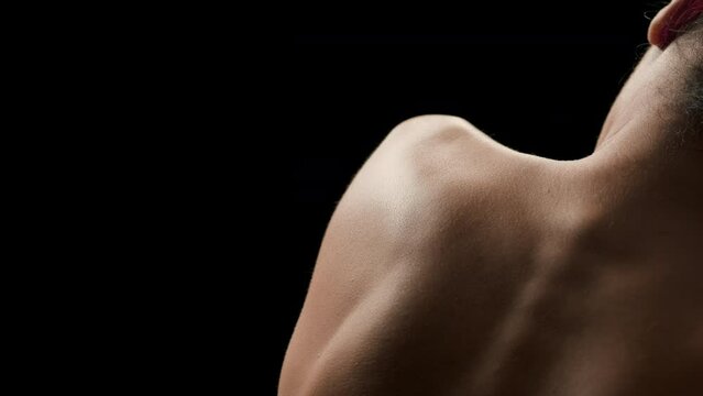 Horizontal close-up shot of young good-looking slim brunette African American woman with curly hair strokes her shoulder blade on black background | Body care concept