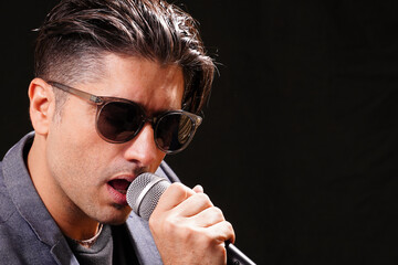 Young man singing holding microphone withblack sunglasses, with a blue jacket and a  black T-shirt...
