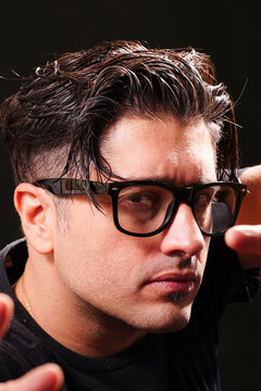 close-up of man with defiant look, looking at camera, wearing black glasses, black t-shirt on black background.