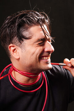 close-up of a man pulling a red cable and its plug connector wrapped around his neck, wearing a black T-shirt on a black background.
