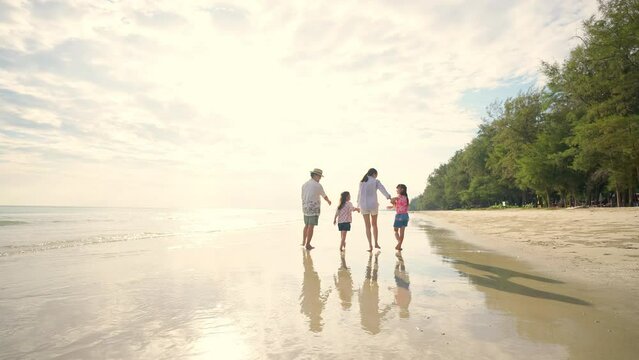 Happy Asian family on beach vacation. Father and mother with two little daughter walking and playing together on the beach at summer sunset. Parents with child girl kid enjoy and fun outdoor lifestyle