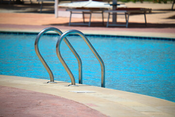 Close up of swimming pool stainless steel handrail descending into tortoise clear pool water....