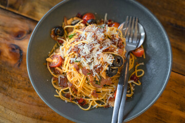 Stir-Fried Spaghetti Pasta with crispy bacon delicious food and dried chili served on a grey ceramic plate on a beautiful wooden table.