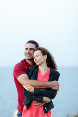 Naklejka premium Portrait of lovely middle-aged couple looking aside at copyspace and hugging while standing at the seaside rock cliff edge.