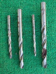 a set of different rusty drill bits for an electric drill lies on a green cloth during the day on...