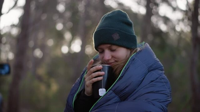 Young woman smelling her tea and looking up outside in morning sun