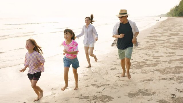 Happy Asian family on beach vacation. Father and mother with two little daughter walking and playing together on the beach at summer sunset. Parents with child girl kid enjoy and fun outdoor lifestyle