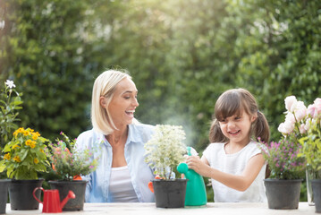 Happy smiling Mother and cute daughter watering and replanting flowers in garden outdoor together.