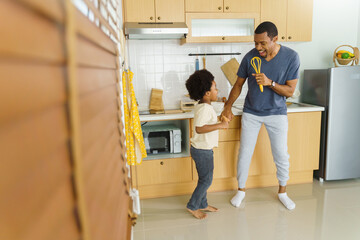 Happy relaxed black African American Father and his little afro boy dancing while cooking in the...