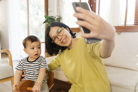 Happy Chinese Young mother and her little son making video chat on using smartphone at home, Asian family taking selfie on mobile phone.
