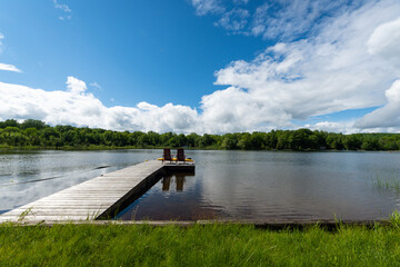 A cottage dock floats out into a lake under a blue sky and white clouds.