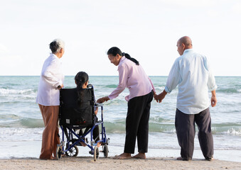 back view senior woman in a wheelchair with friends enjoy travel on the beach