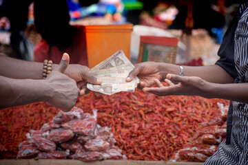 Naklejka na ściany i meble Two African hands of a seller and buyer exchanging money, cash, currency or naira notes in a market place during transaction