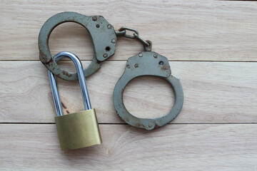 Metal padlock with steel police handcuff isolated on wooden background closeup.