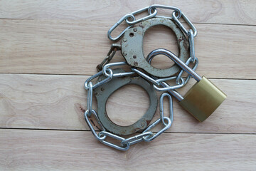 Metal padlock and steel chain with rusty handcuffs isolated on wooden background closeup.