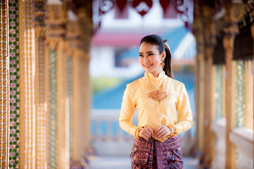 Fototapeta premium Portrait of a beautiful woman wearing a traditional Thai dress smiling gracefully standing in a temple of Thailand