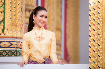 Portrait of a beautiful woman wearing a traditional Thai dress smiling gracefully standing in a temple of Thailand